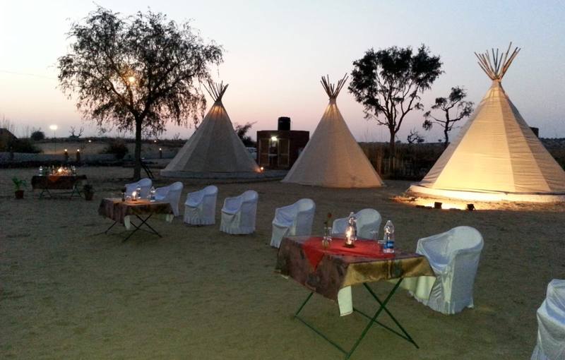Tipi-style tents lit at dusk with dining tables